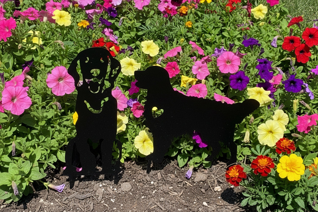 Two metal garden stakes in a garden, one in the shape of a dog sitting and the other in a standing pose with a heart cut out.